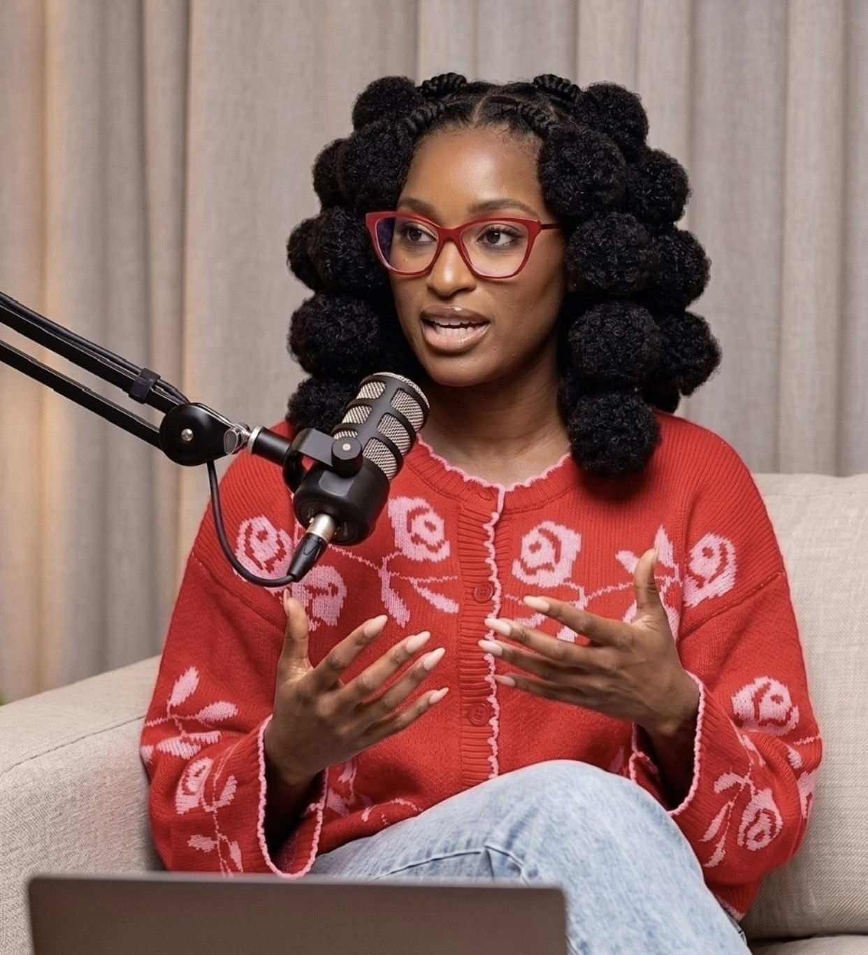 Shiloh speaking into a podcast microphone in a red floral sweater