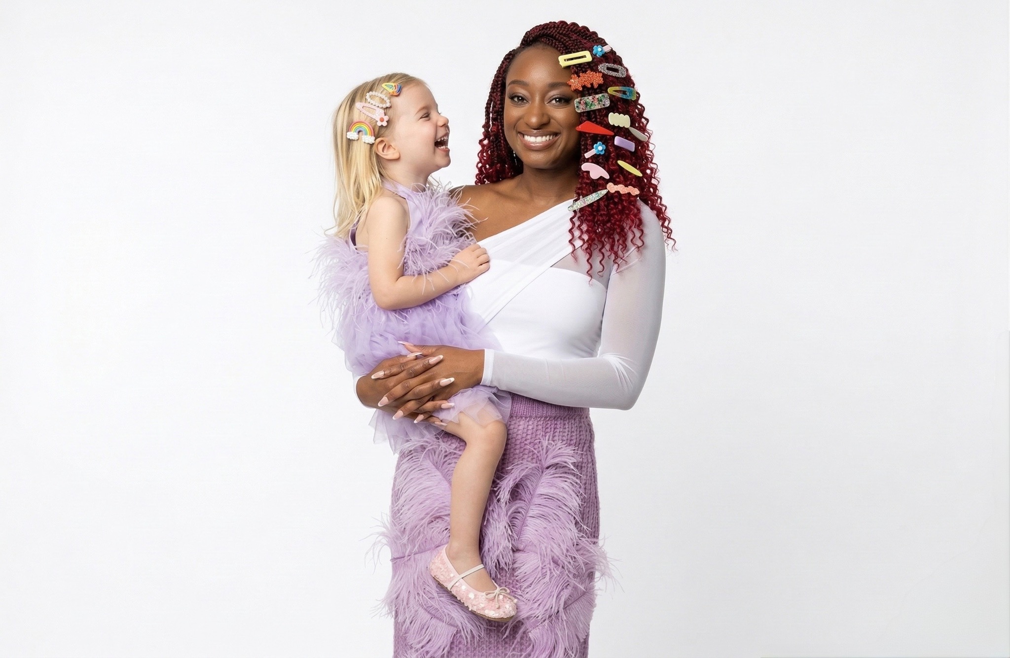 Shiloh smiling while holding a laughing child, both wearing colorful hair clips